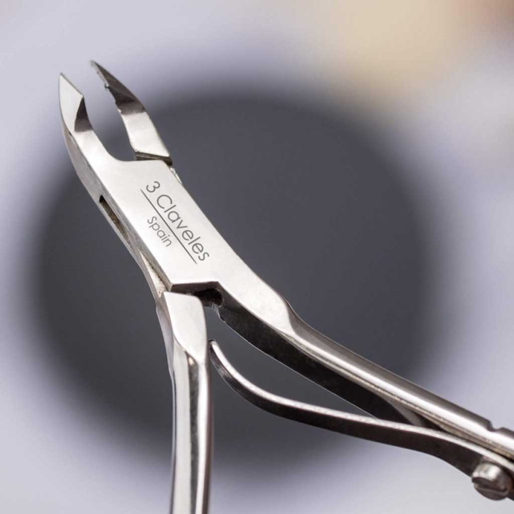 Metal cuticle nipper with '3 Claveles' branding on a blurred background
