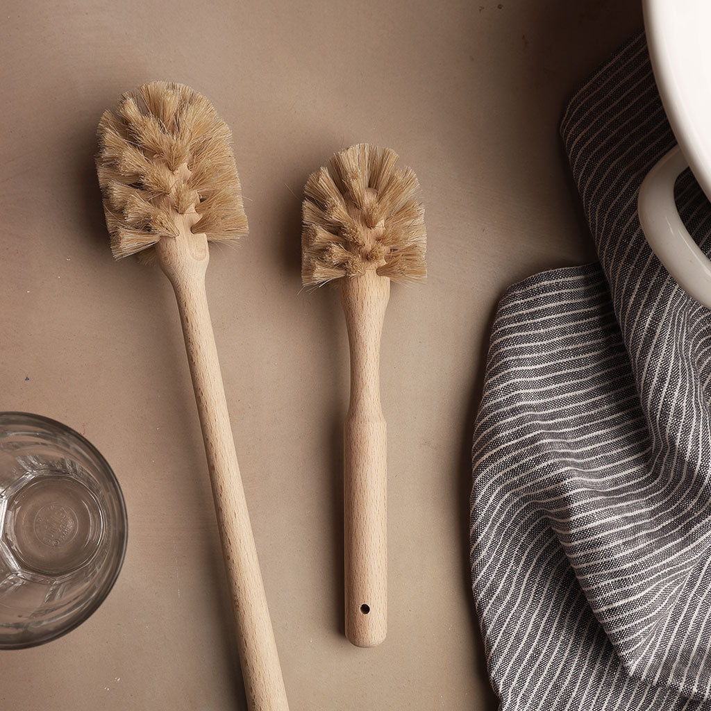 Two wooden scrub brushes on a beige surface with a striped towel and a drinking glass.