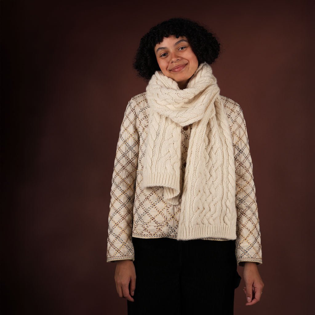 Person wearing a patterned jacket and cream scarf against a brown background