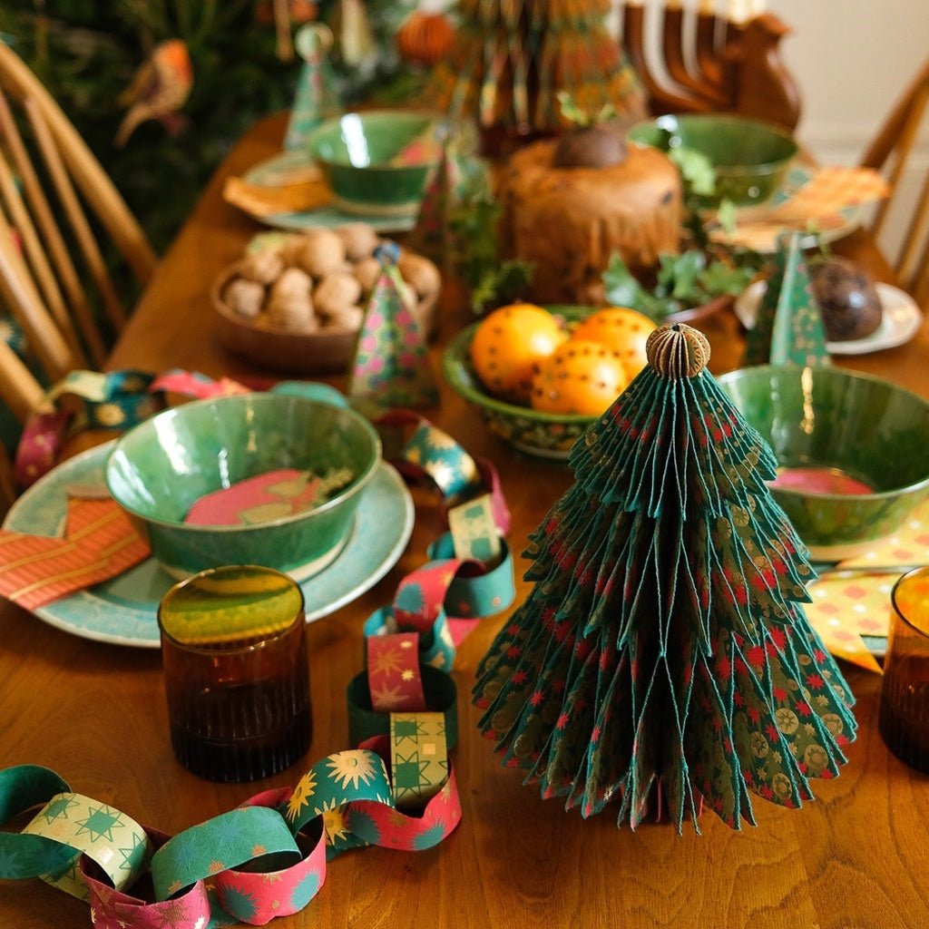 Paper tree decoration on table around place settings and decor items.