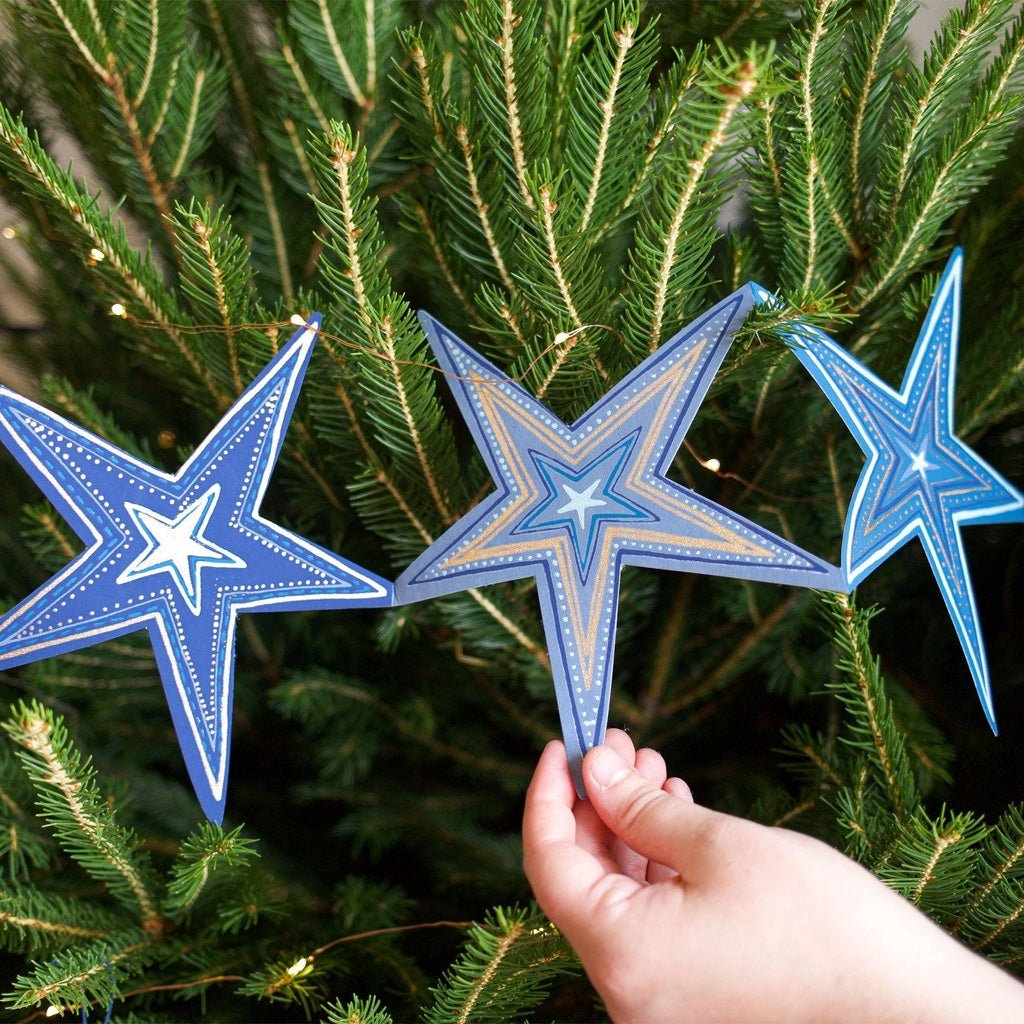 Hand touching blue star garland hanging on green Christmas tree.