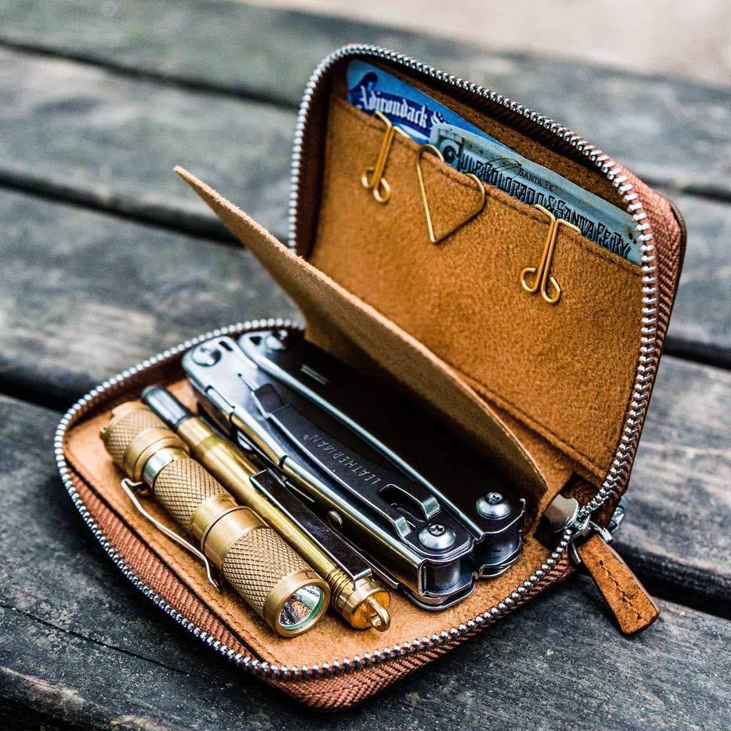 Brown leather wallet with tools and a flashlight on a wooden surface
