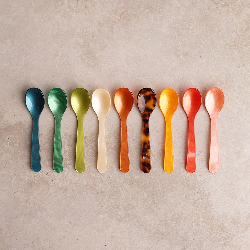 Row of colored acrylic egg spoons on light background