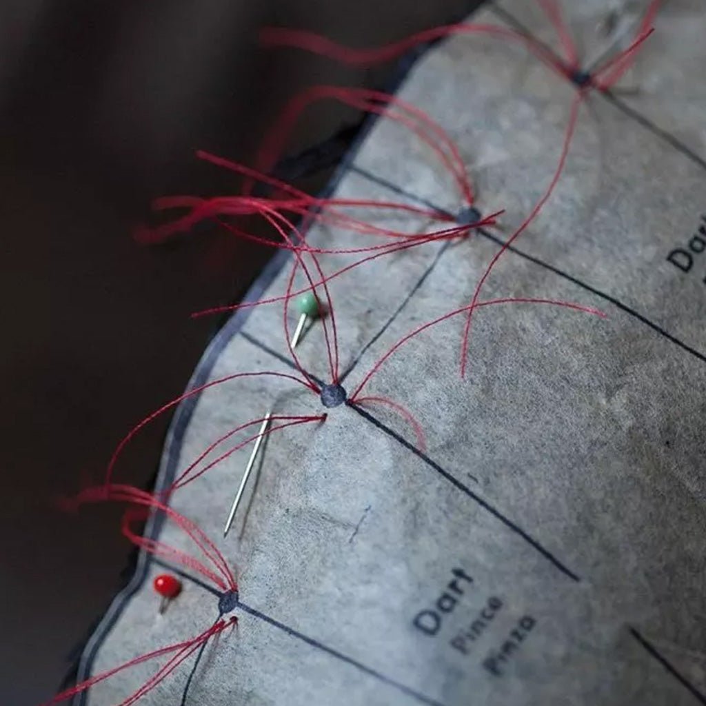 Close-up of sewing pattern with darts, pins, and red thread