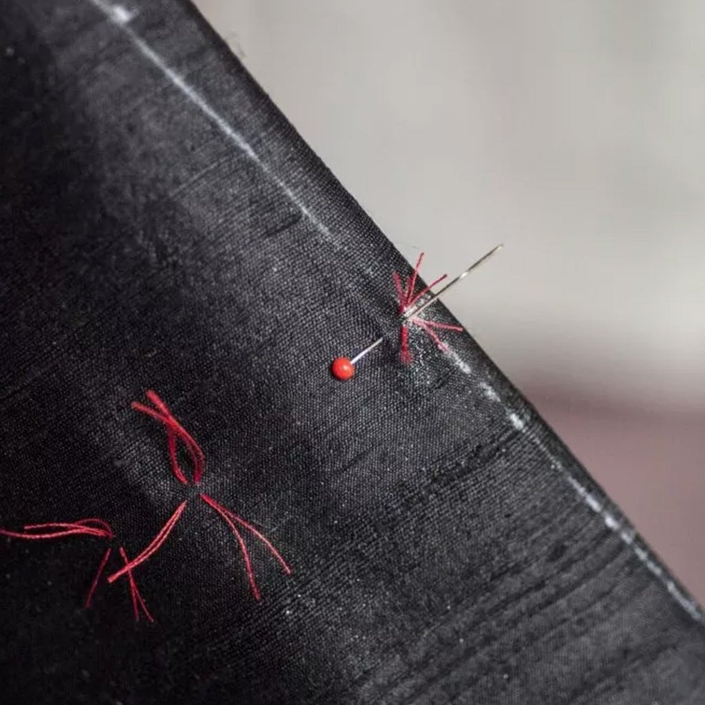 Black fabric with red thread, tailor's chalk, and a needle on a neutral background