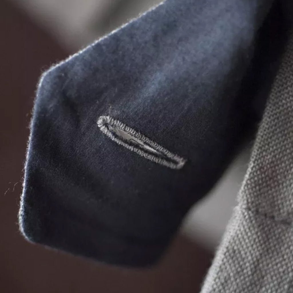 Close-up of a button hole on dark blue fabric with a subtle pattern.