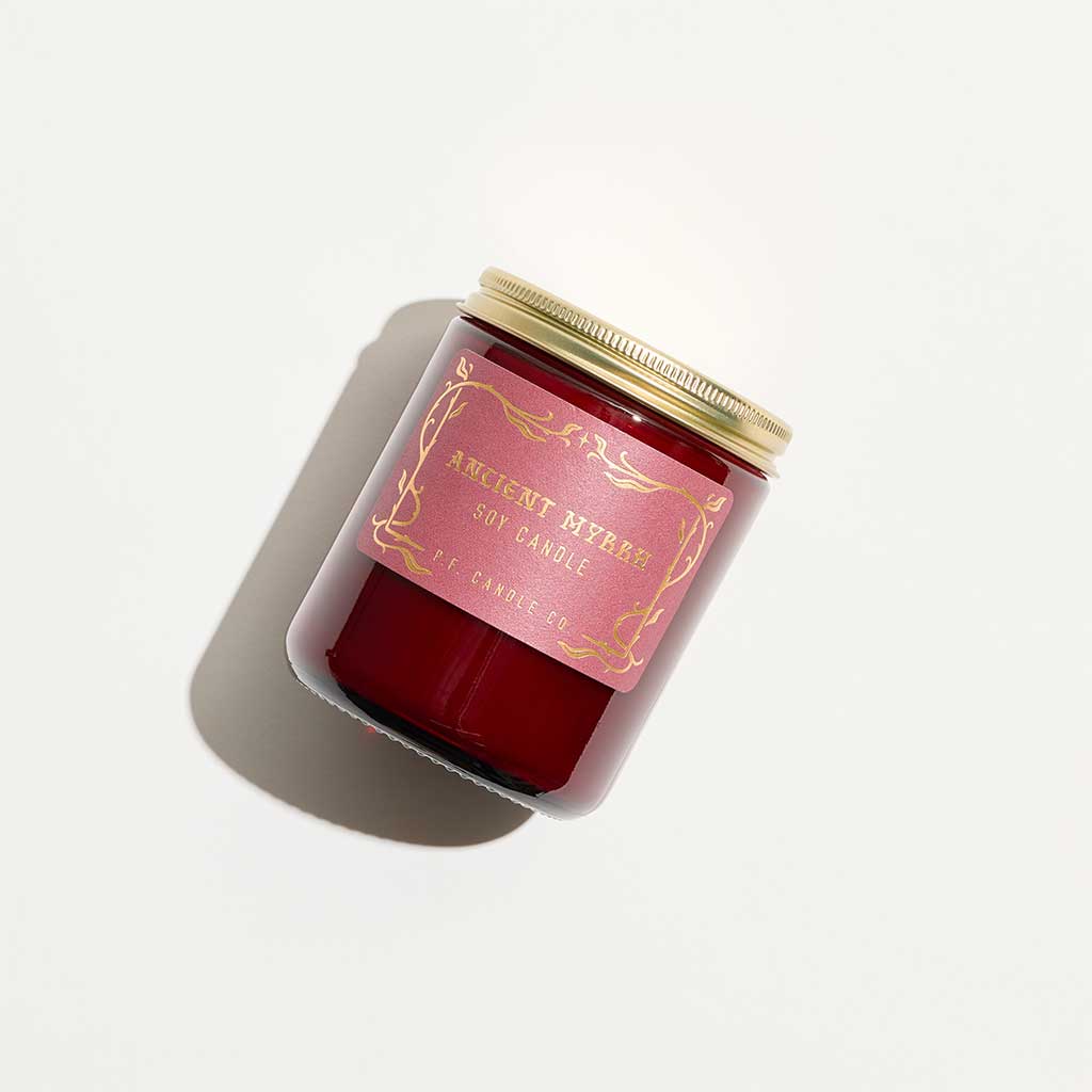 Red candle in a decorative container with a gold lid on a light gray background
