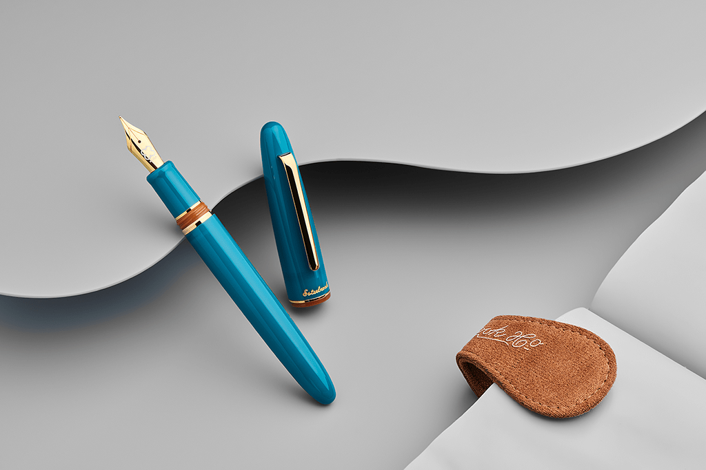 Blue fountain pen with gold accents on a gray surface, accompanied by a brown leather pouch.