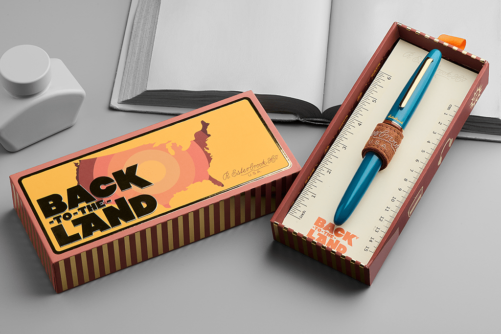Blue pen in a decorative box with 'Back to the Land' packaging on a gray surface.