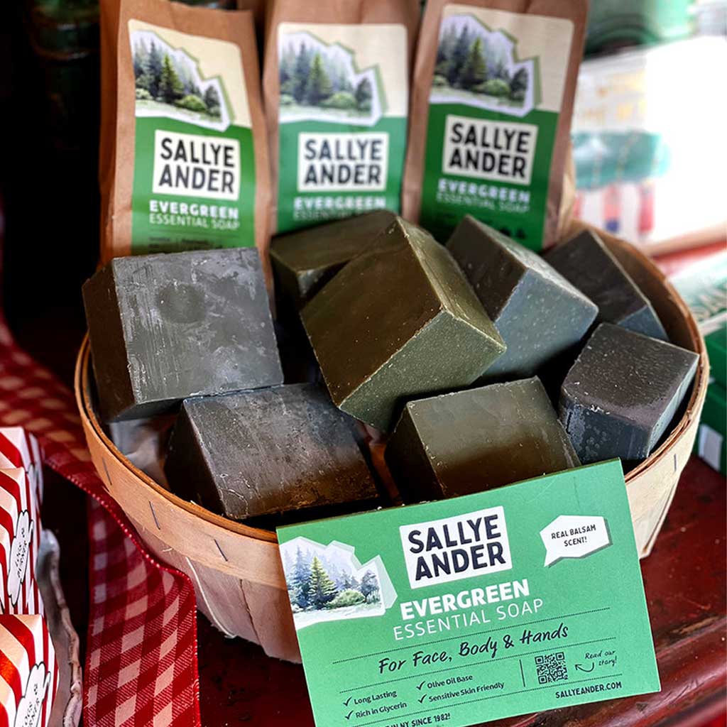Wooden basket of blocks of Dark green SallyeAnder evergreen essential soap next to packaging on table