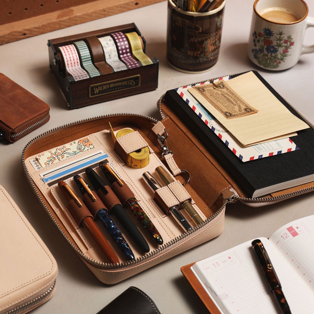 Leather expansi-folio zip folio in undyed color with pens and stationery supplies on desk.