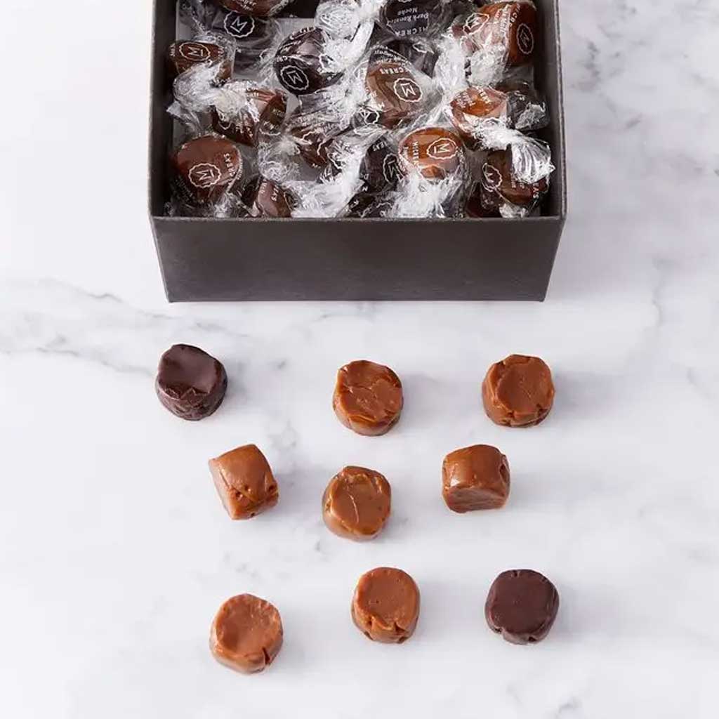 Box of wrapped caramels with some unwrapped on a marble surface