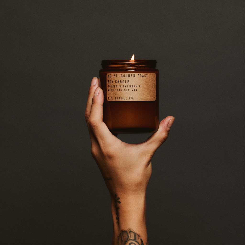 Hand holding a lit amber candle against a dark background