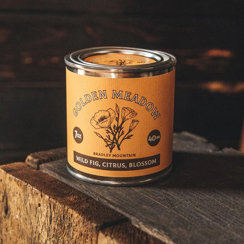 Candle in a tin labeled 'Golden Meadow' by Bradley Mountain on a wooden surface.