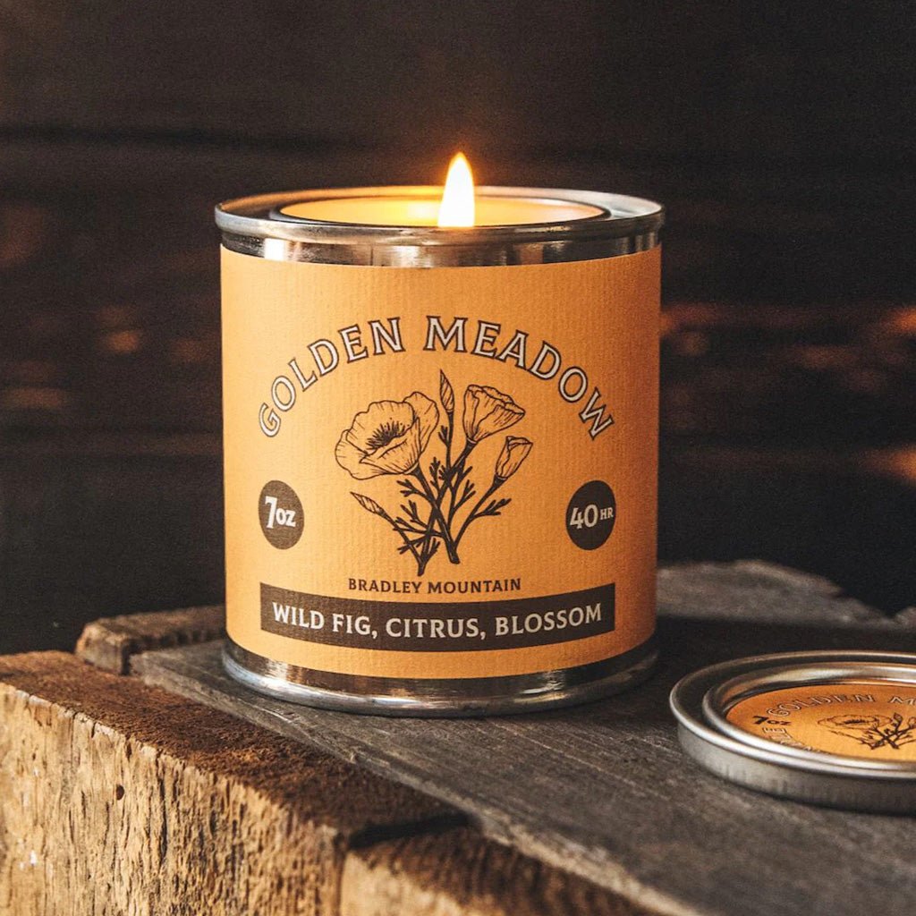 Candle in a 'Golden Meadow' tin on a wooden surface with a dark background