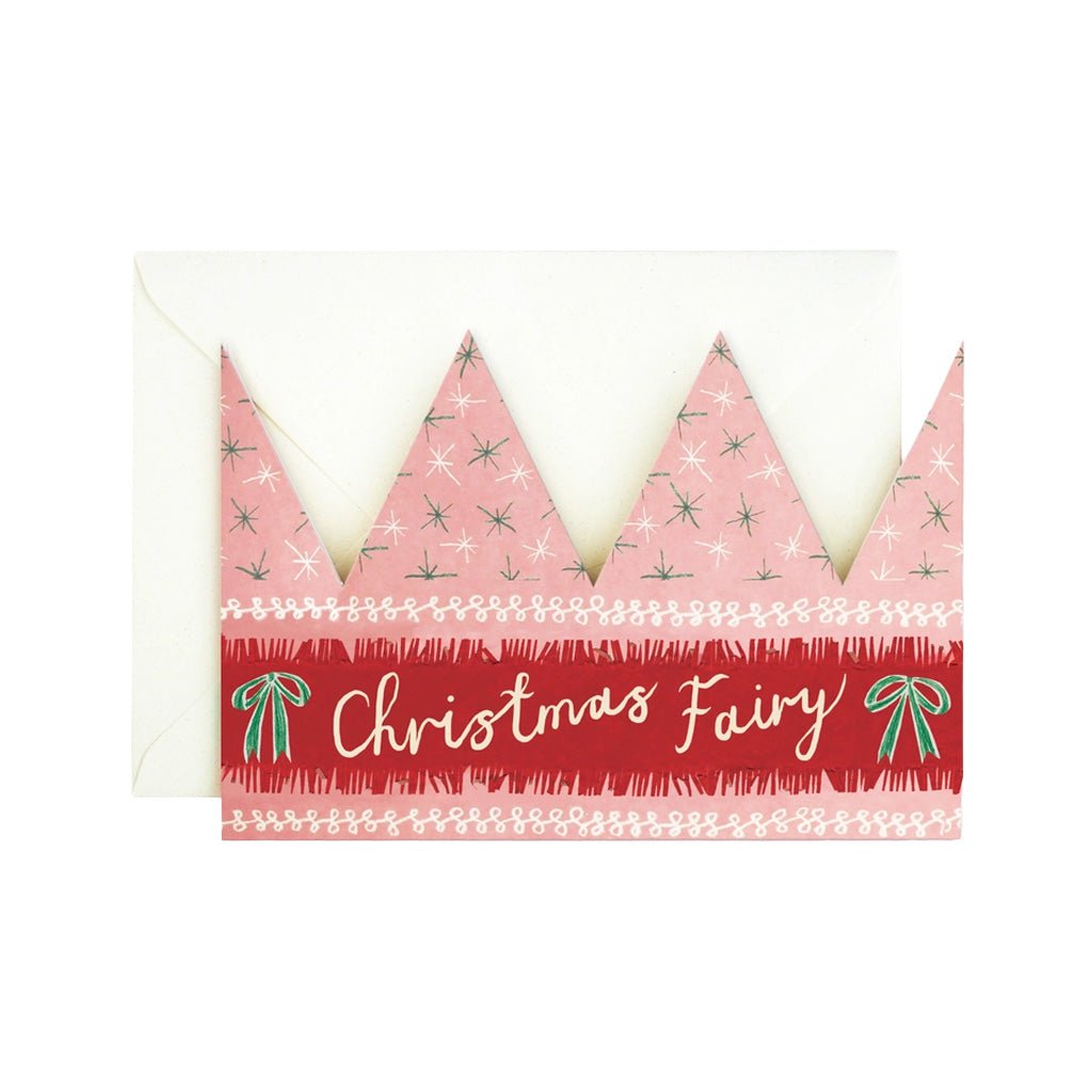 A Christmas-themed greeting card featuring a pink crown with green pine tree patterns and a red banner reading 'Christmas Fairy' in white script, shown with a white envelope on a white background.