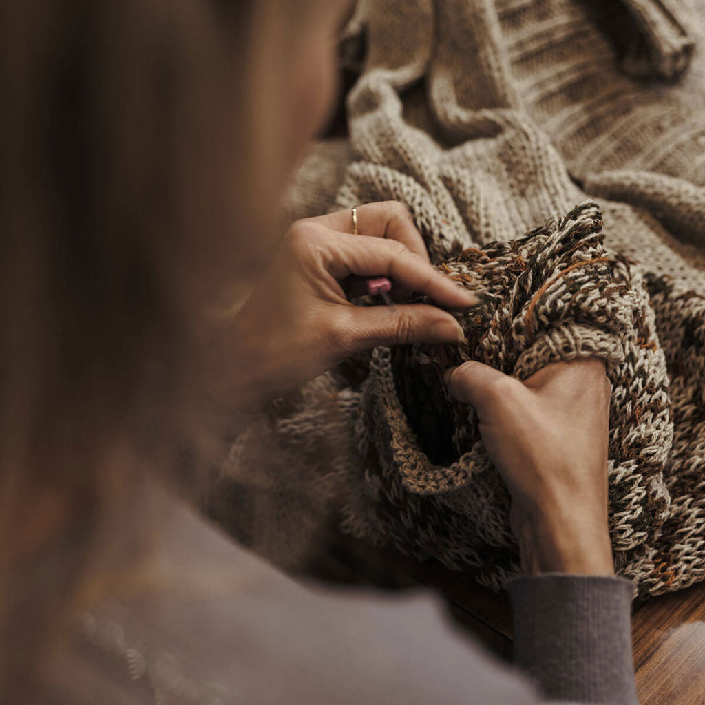Close-up of hands holding a knitted item with a textured blanket in the background.