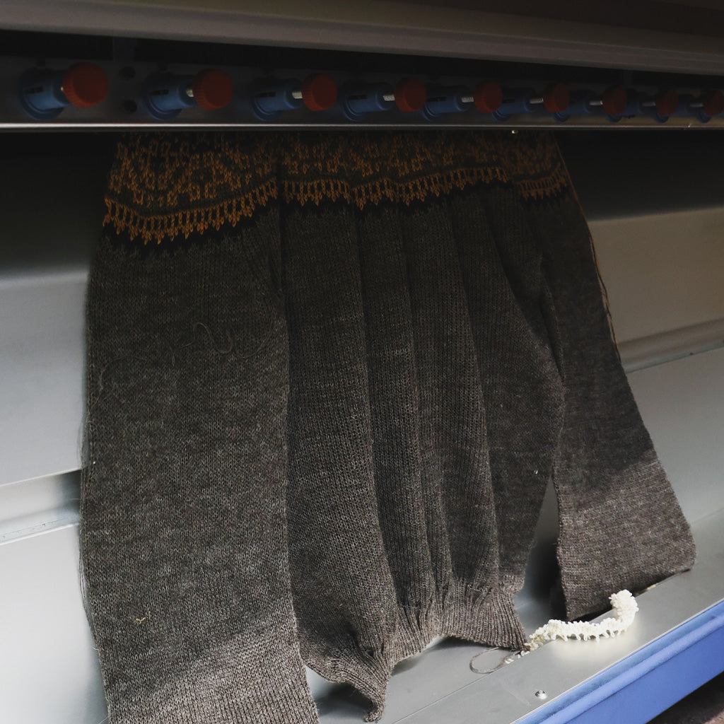 A knit sweater emerging from knitting machine.