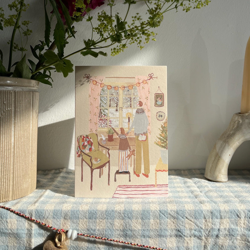 A holiday card standing upright on table surrounded by ceramics.
