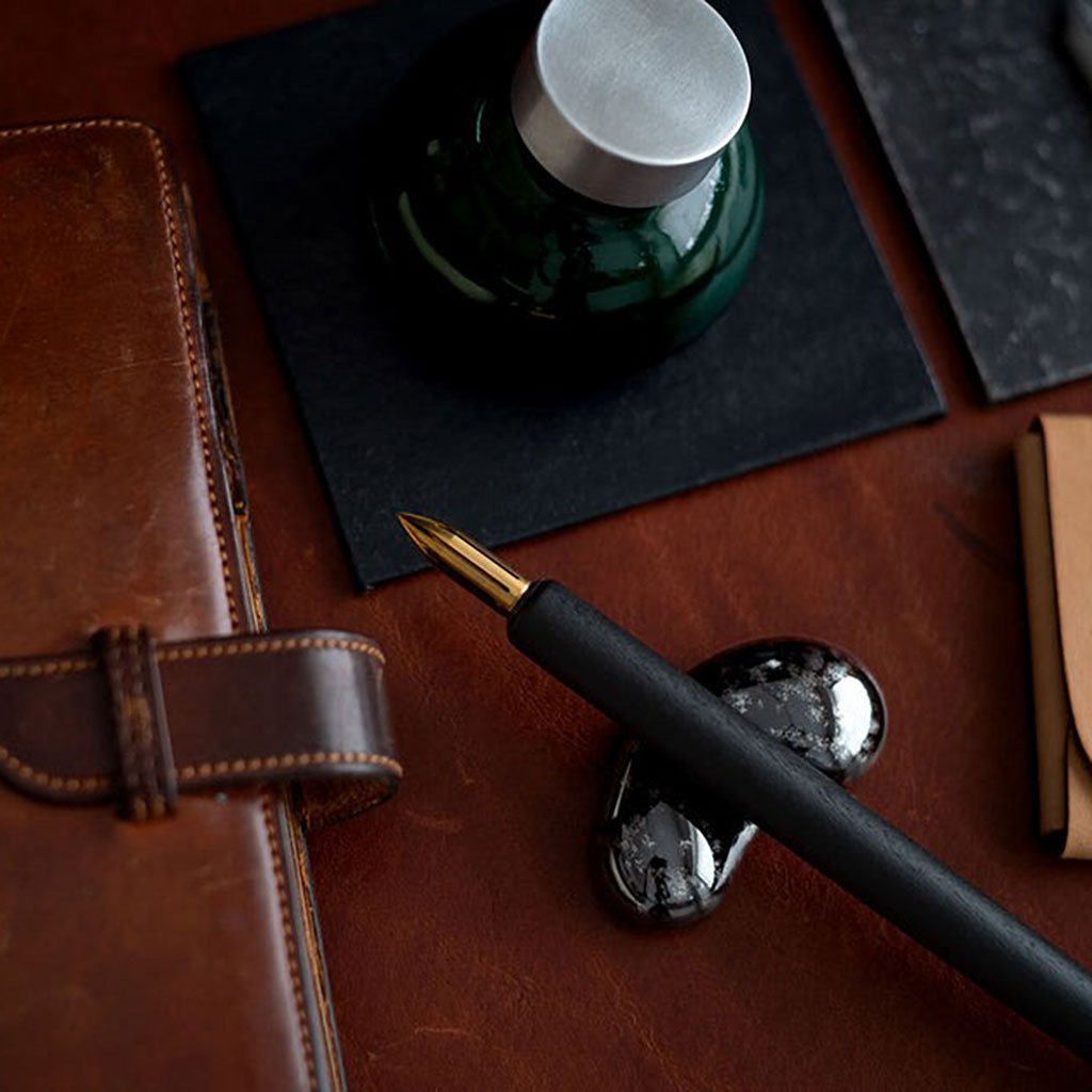 Pen on black pen rest and ink bottle on a leather surface with a bottle cap