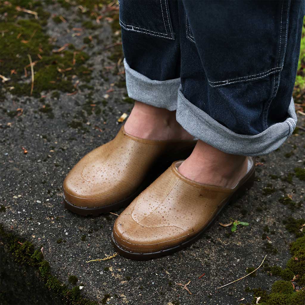 Brown hemp mules worn with rolled-up jeans on a wet pavement.
