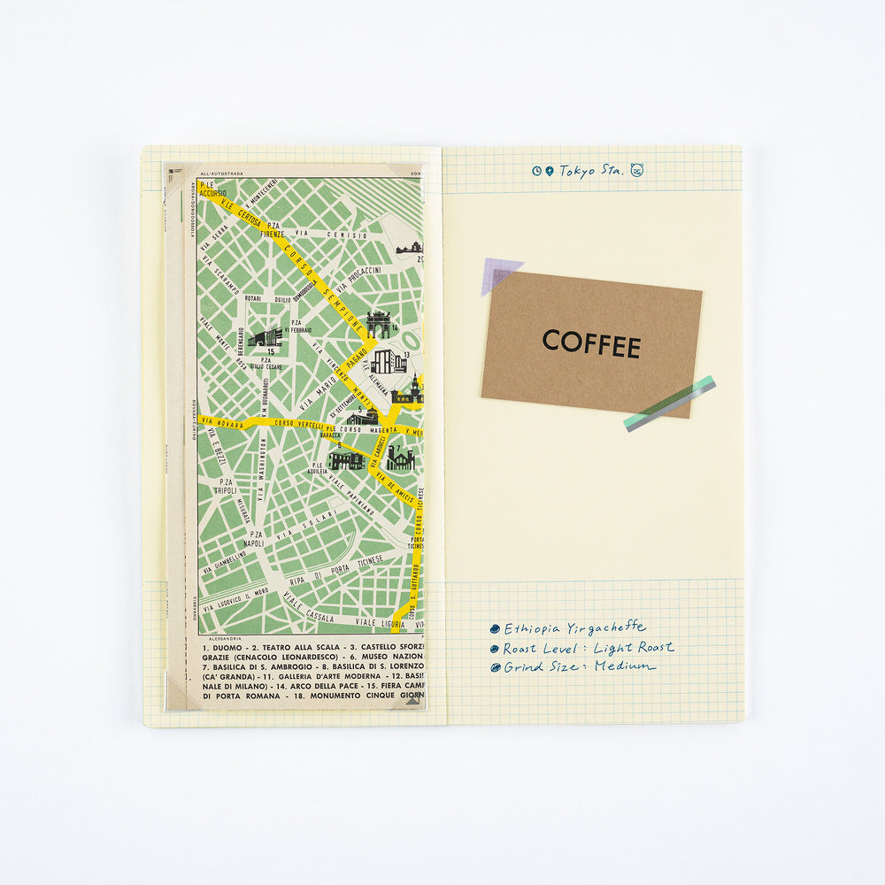 A flat-lay view of a Japanese-style travel map notebook or journal, showing a green street map on the left page and handwritten notes on the right page with a brown paper 'COFFEE' label.