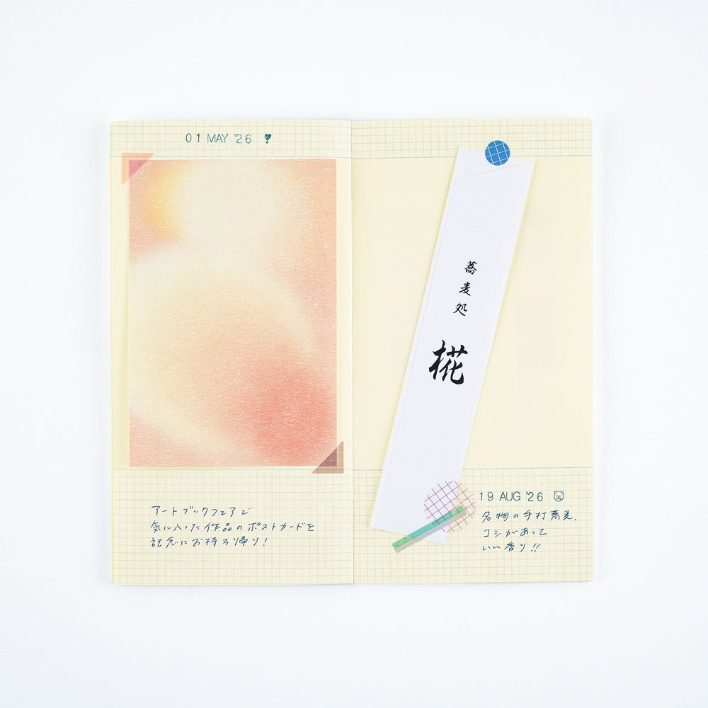 A pocket notebook with a cream-colored grid page, featuring a pastel peach watercolor illustration on the left, handwritten notes in Japanese, and a white bookmark with black calligraphy.