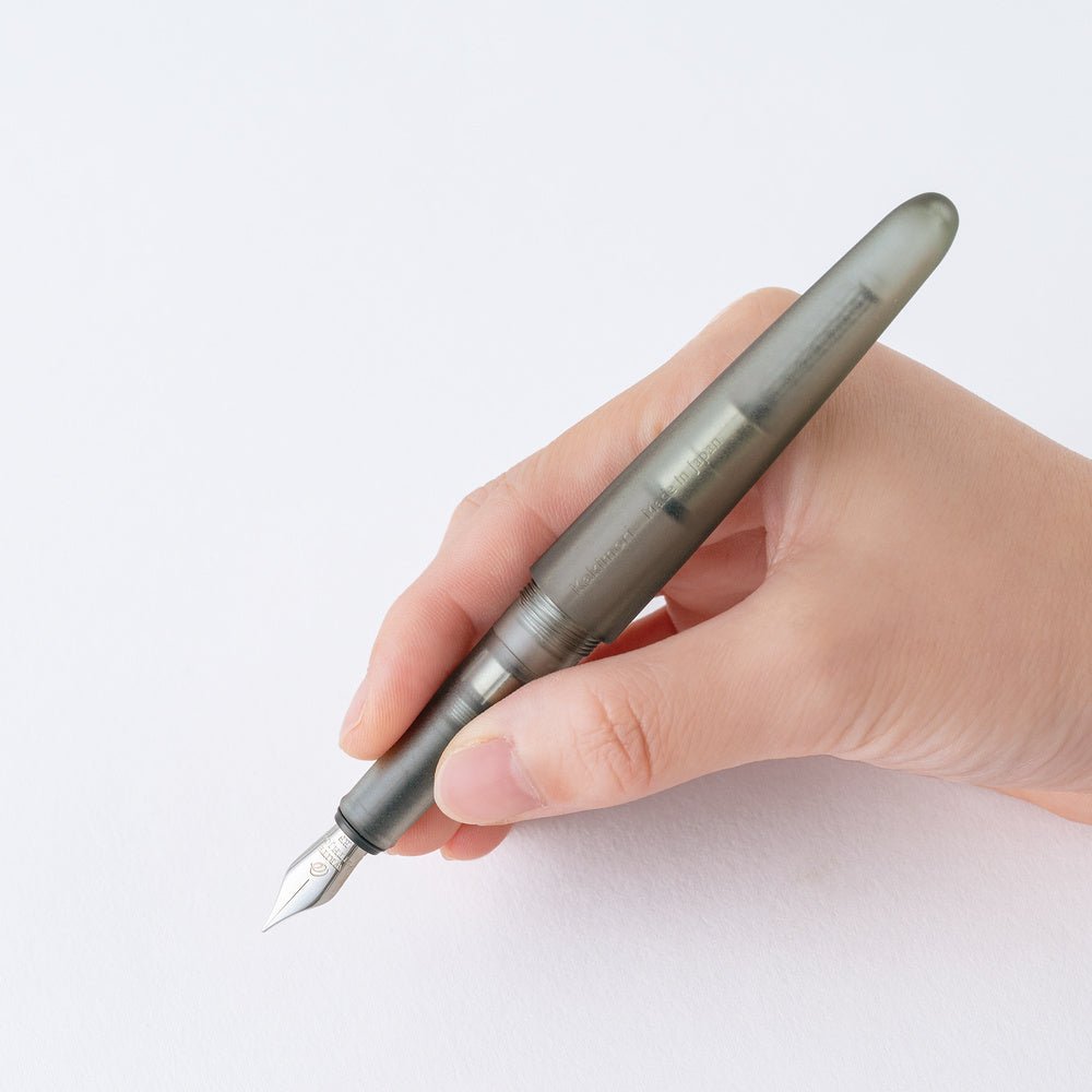 A hand holding a translucent gray fountain pen with a silver nib against a clean white background.