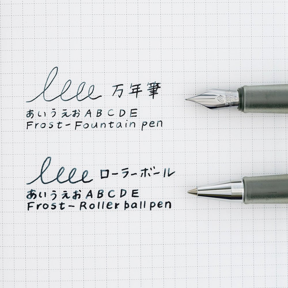 Two pens, one with a fountain pen nib and one with a Rollerball nib, shown on a white graph paper background with sample handwritten Japanese text and English transliterations.