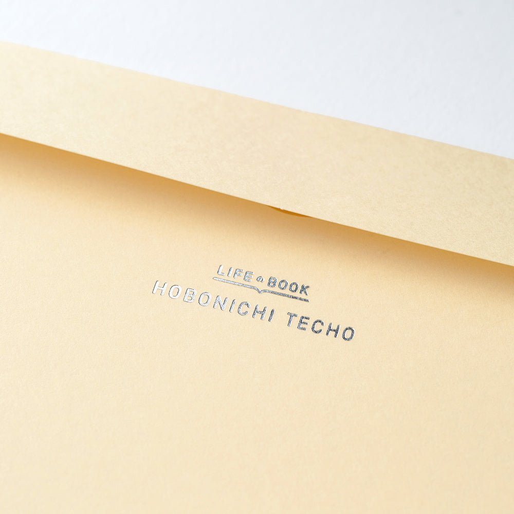 A close-up of a light beige paper envelope with the text 'LIFE BOOK' and 'HOBONICHI TECHO' printed in silver on the flap.