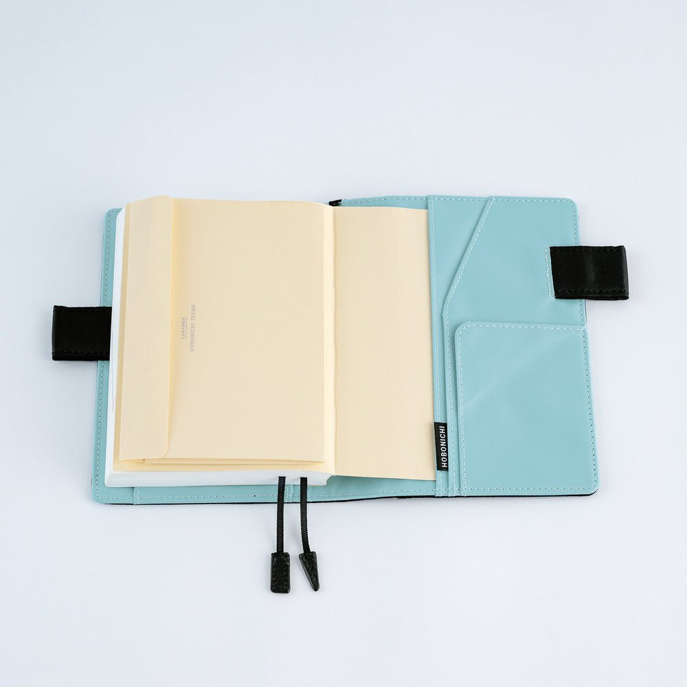 An open light blue planner or notebook cover with cream-colored pocket envelope inserted, shown on a clean white background.