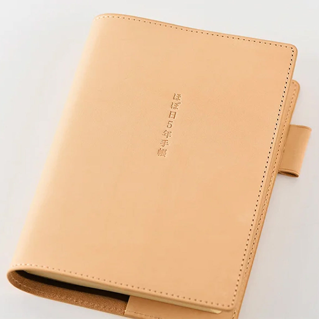 A tan leather planner cover with vertical Japanese text printed on the front, photographed on a clean white background.