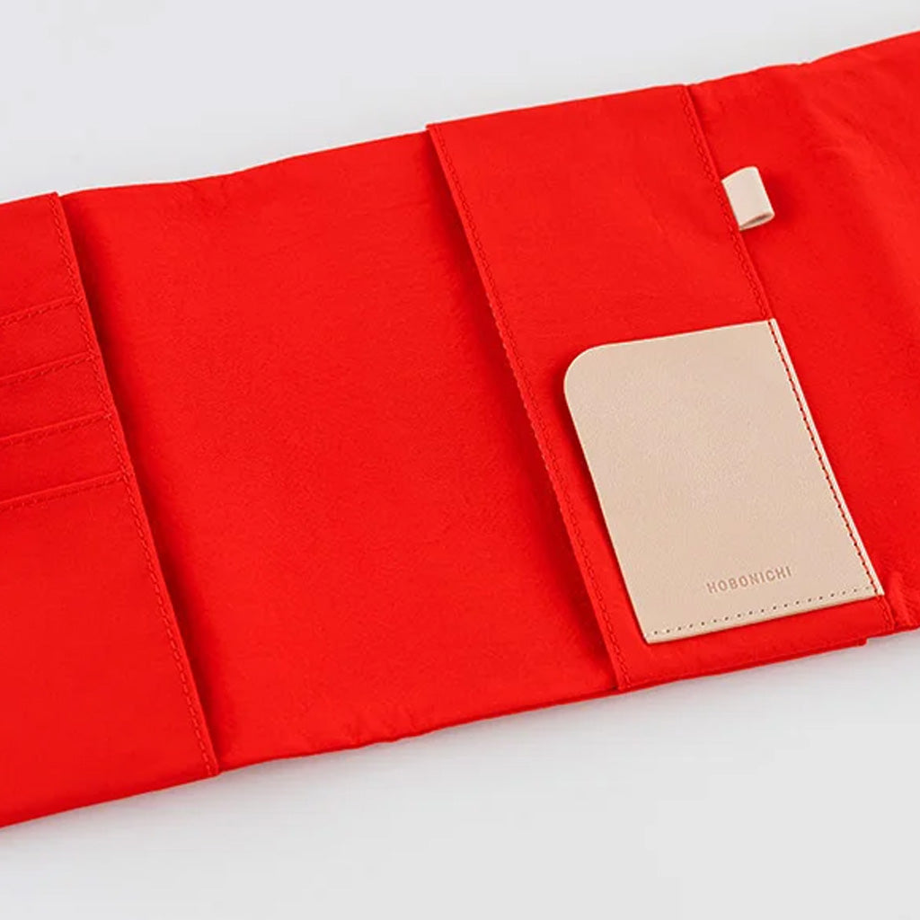A bright red fabric organizer pouch shown open on a white background, with a beige leather brand patch reading HOBONICHI attached on one side.
