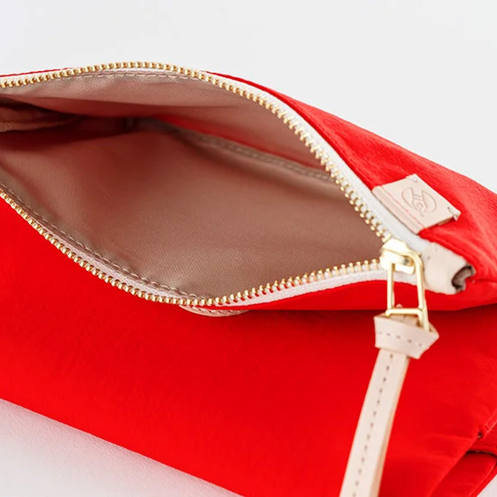 Close-up of a bright red zippered pouch with a light beige interior lining, gold-tone zipper teeth, and a small beige brand tab near the zipper.