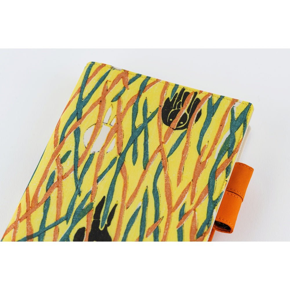 Close up of front of Hobonichi Unsodo A5 Cousin Book in yellow cover with white and black rabbits under abstract orange and blue linear design and two orange pen loops on white background