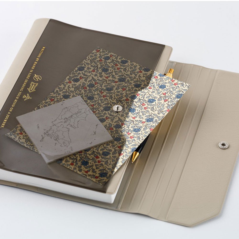The outside transparent front pocket of a Hobonichi Alettone cover holding a piece of floral paper and a map sticky note. Gold text on the front cover says, 'Writing by hand is like sending your mind on a journey.'