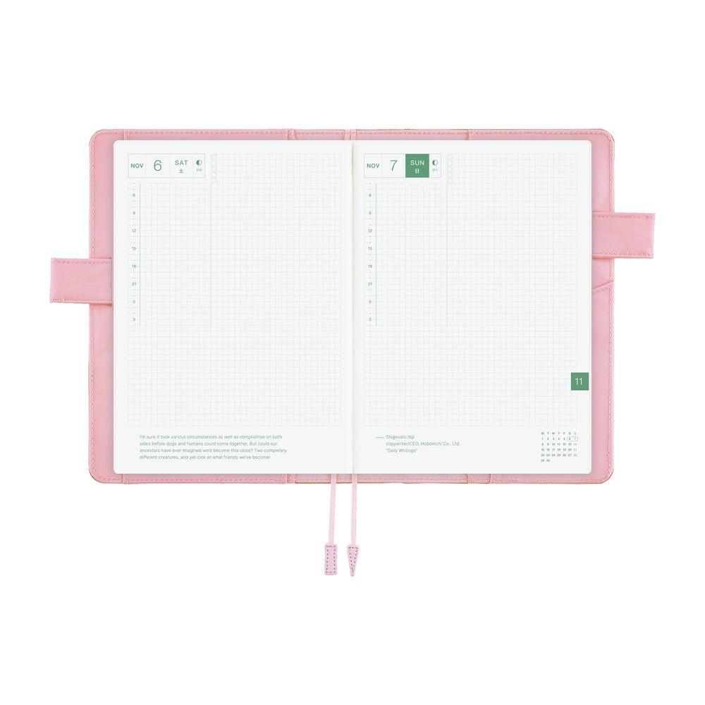 An open pink planner with white grid pages, ribbon bookmarks, and side loops, photographed on a clean white background.