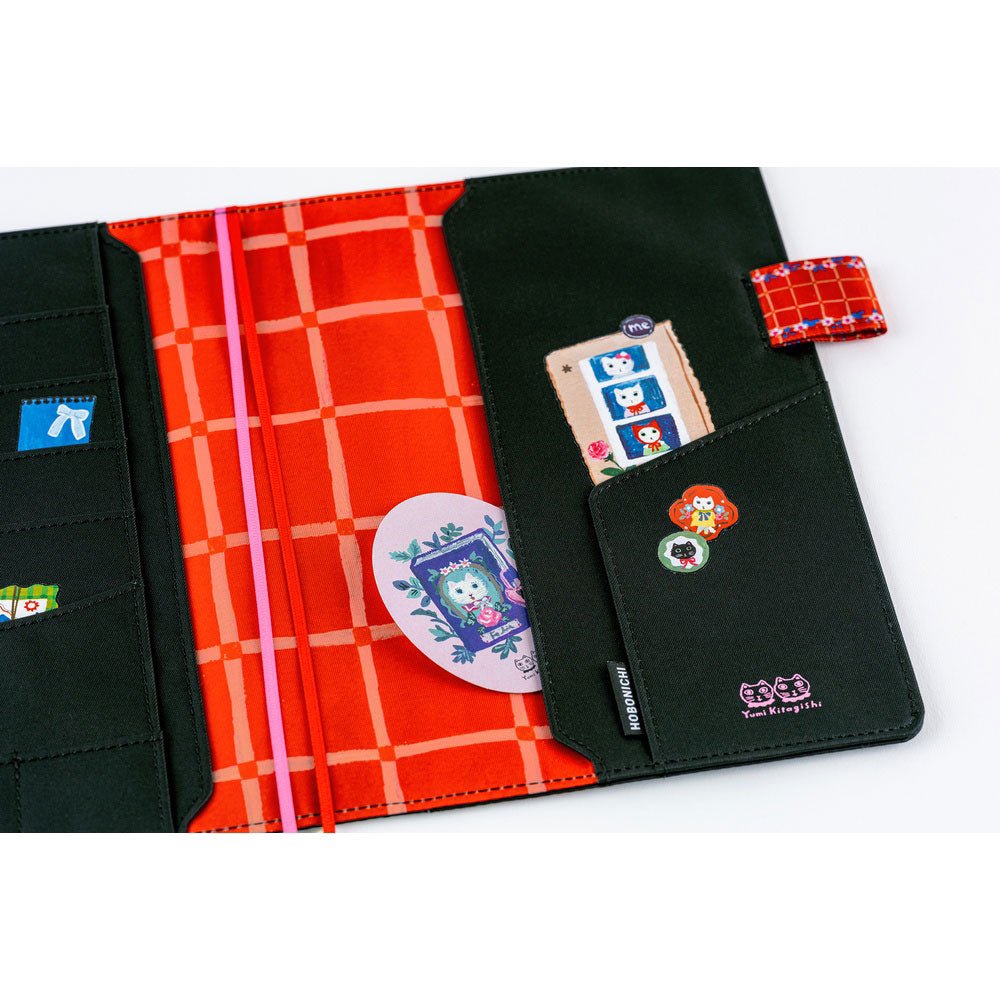Interior details of a black Hobonichi Techo with whimsical cat illustrations. The inside cover features bright red grid fabric and black contrasting fabric, illustrative details, and several pockets.