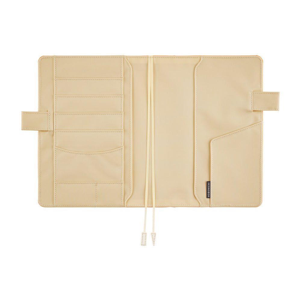 Ivory interior of a Hobonichi Techo cover laid open flat on a white background, showing multiple card and storage pockets, pen loops, and two ribbon bookmarks.