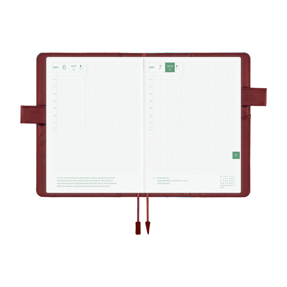 An open planner with white grid pages and a dark reddish-brown interior cover, shown on a plain white background. The cover has a pen loop on both sides and two ribbon bookmarks hanging from the bottom center.