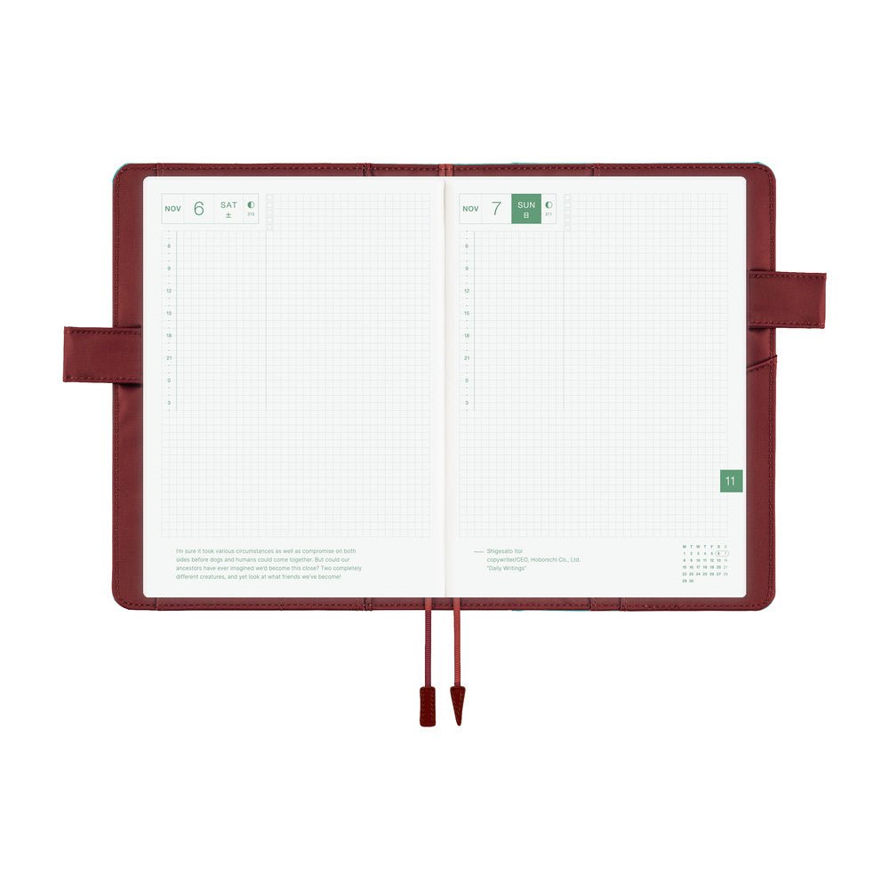 An open planner with white grid pages and a dark reddish-brown interior cover, shown on a plain white background. The cover has a pen loop on both sides and two ribbon bookmarks hanging from the bottom center.