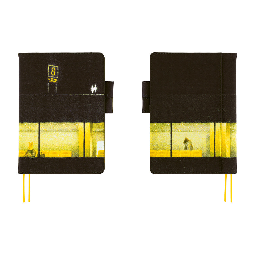 Two side by side views of yellow and black planner cover featuring a graphic of an airport with a glowing yellow window and a sign with the number 8. The notebook has two yellow ribbon bookmarks and is shown against a solid white background.