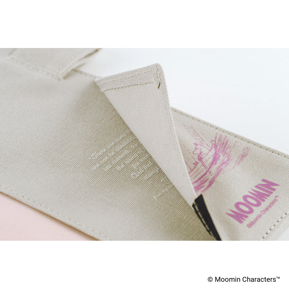 Close-up interior image of a beige cover with a folded corner revealing printed text and a pink line-art illustration. The word 'MOOMIN' is printed in pink on the inside.