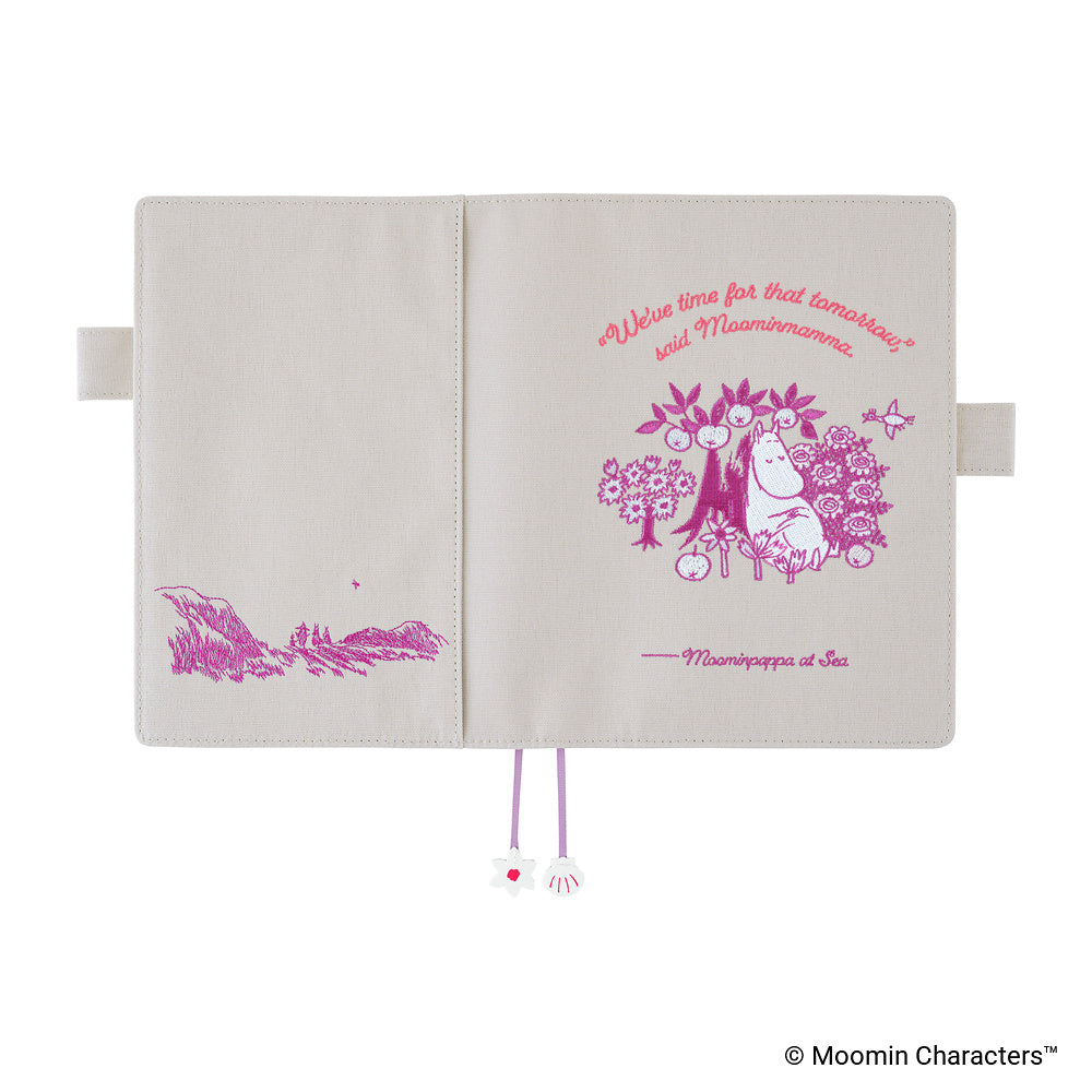 An open Moomin Characters planner cover on a white background, showing a cream-colored cover with pink illustrations and text as well as ribbon bookmarks featuring a flower and shell. The front cover features a Moomin character illustration with the quote 'We'll see for that tomorrow!'