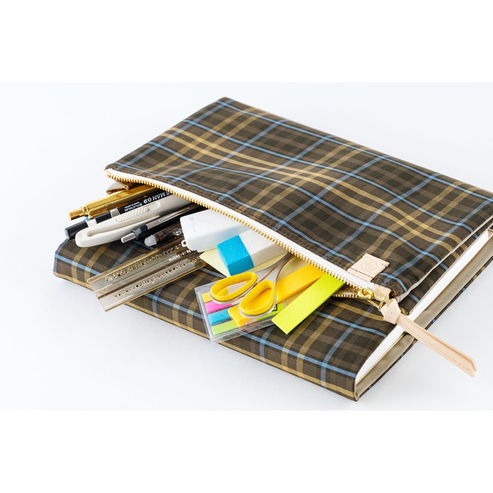 An exterior Hobonichi Techo cover zipper pocket with a brown and beige plaid pattern, shown open with stationery items like pens, a ruler, sticky notes, and scissors peeking out against a white background.