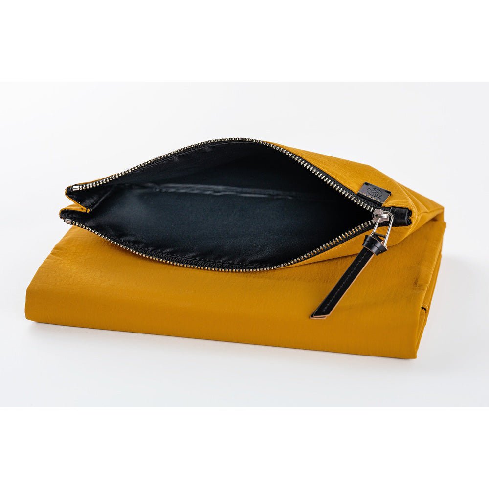 Close-up of the open zippered pouch on a mustard yellow Hobonichi Tragen cover, showing its black interior and black zipper pull on a white background.