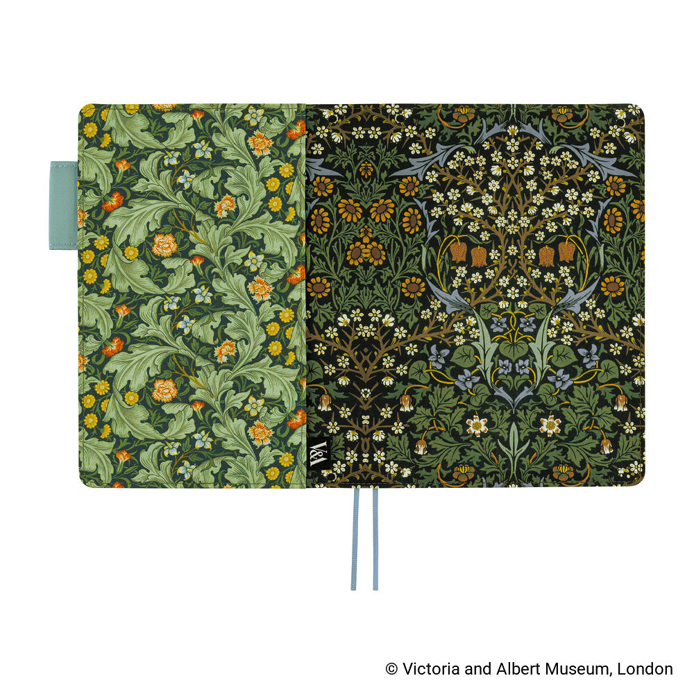 A Hobonichi Techo cover with a floral pattern, shown open against a white background. The left (back) panel has green leaves and orange flowers, while the right (front) panel has a black background with white flowers.