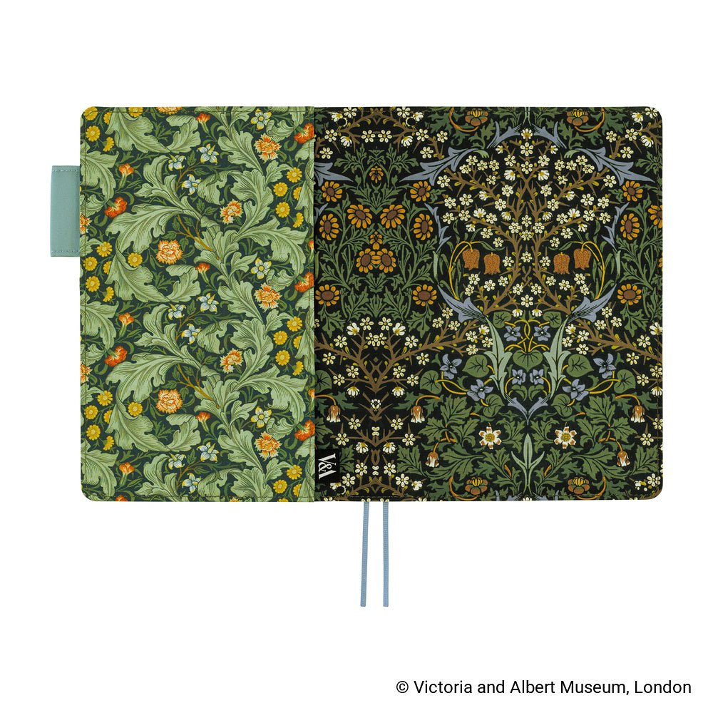 A Hobonichi Techo cover with a floral pattern, shown open against a white background. The left (back) panel has green leaves and orange flowers, while the right (front) panel has a black background with white flowers.