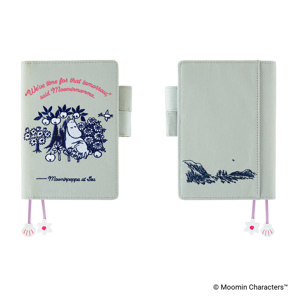 A Moomba-style planner or notebook shown from two angles on a white background. The cover is a very pale mint green with dark blue line art of Moomba and pink script text on the front, plus a small pink-and-white flower bookmark charm.