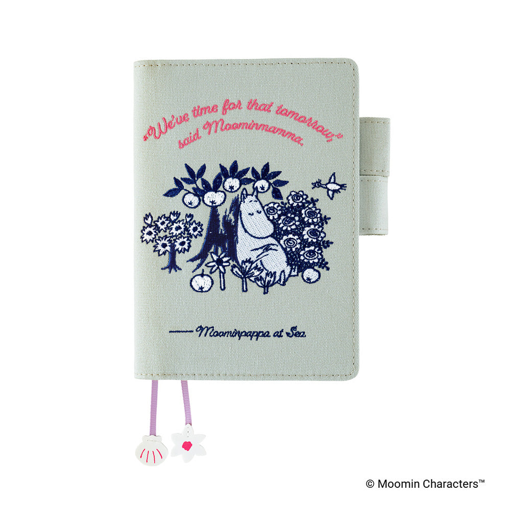 A Moominmamma journal cover featuring a navy blue illustration of Moominpappa at sea and pink cursive text, on a light sage green background with a matching strap and decorative tags.